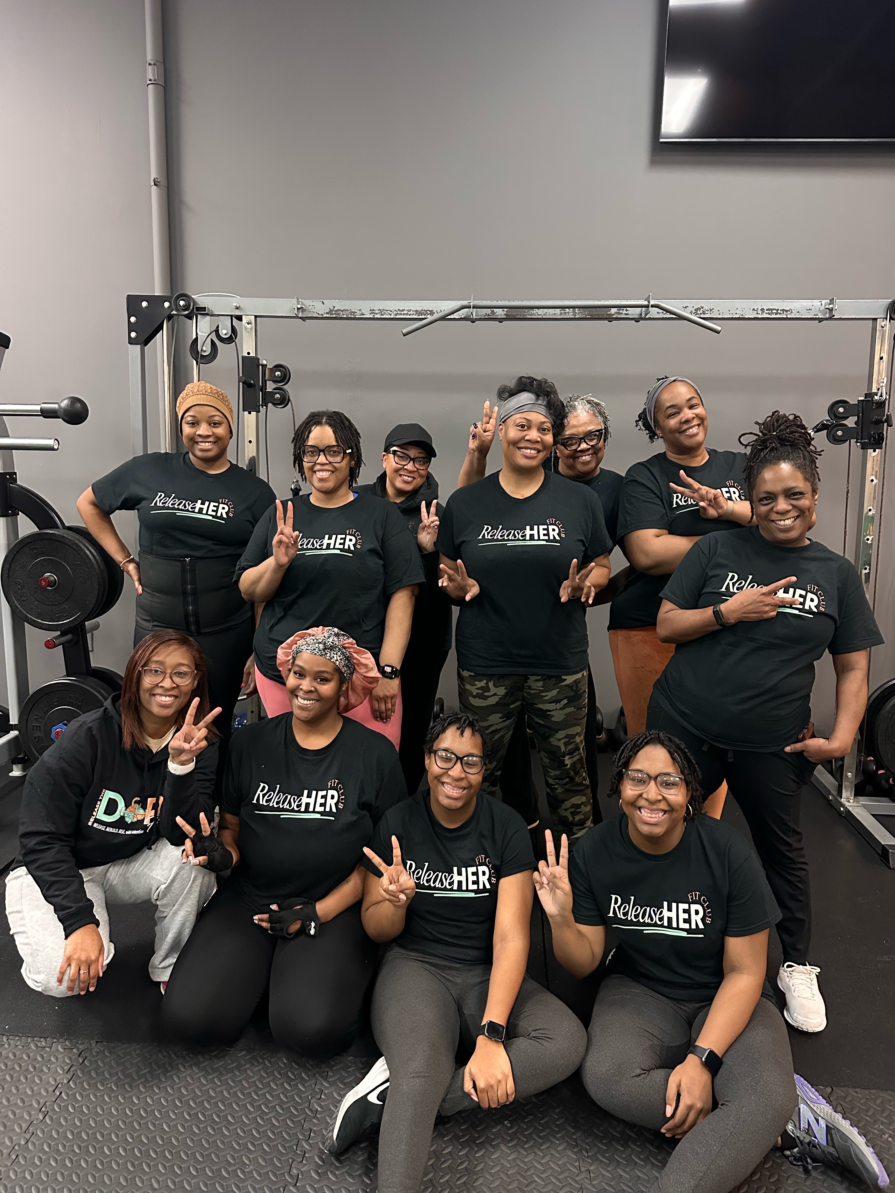 ReleaseHER Fit Club members in black t-shirts posing together at the gym